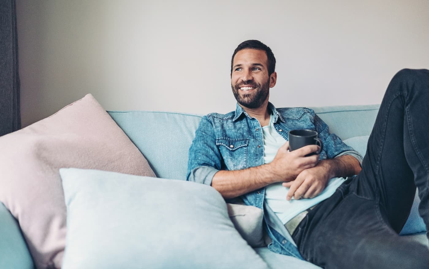 Man relaxing comfortably on a couch with a cup of coffee — the calm and safety that trauma therapy at MMHC helps restore